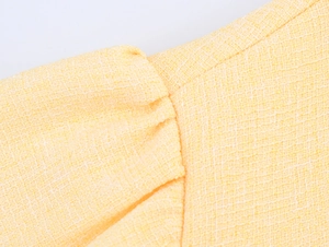 Dettaglio del tessuto in tweed giallo e delle cuciture sulla spalla del vestito