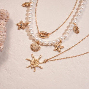 Close-up of gold layered necklace set with pearls, starfish and shell pendants