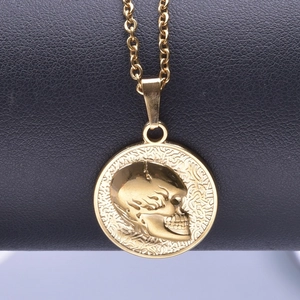 Macro detail of gold stainless steel necklace featuring a relief skull on a coin pendant
