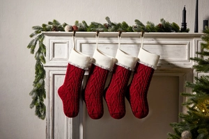 Close-up of knit Christmas stockings with heart patterns hanging on a cozy white fireplace