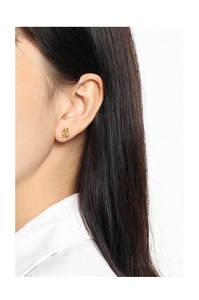 Close-up of minimalist golden bear stud earrings shown worn on a model's earlobe