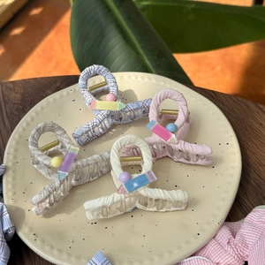 Detail of fabric-wrapped hair claws with pencil charms and beads on a ceramic plate