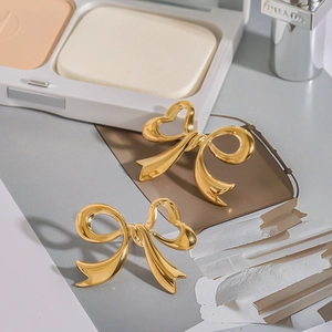 Detail shot of golden bow heart stud earrings with luxury makeup accessories on gray background