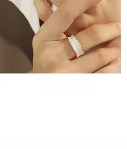 Detail of a wavy gold stainless steel ring with white enamel inlay worn on the finger