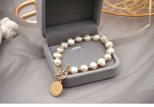 Detailed macro of baroque pearl bracelet with gold coin charm in gray velvet gift box