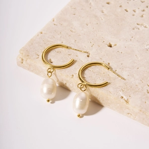 Elegant gold hoop earrings with natural baroque pearls on a white stone background
