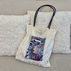 Detail of cream canvas tote bag featuring colorful artistic floral print and black rope straps