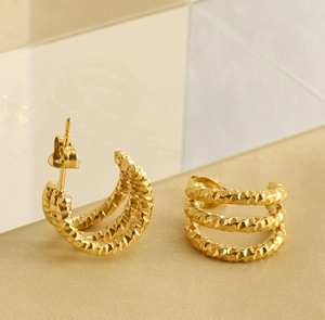 Detail view of triple-row gold C-shaped earrings with hammered texture on a neutral surface