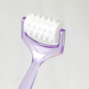 Macro detail of white textured roller head and purple translucent handle massage tool
