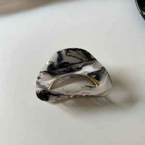Detail view of black and white marble acetate hair claw clip with golden metal spring