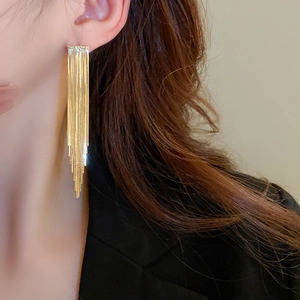 Close-up of elegant gold tassel earrings with tiered metal rods on a female model
