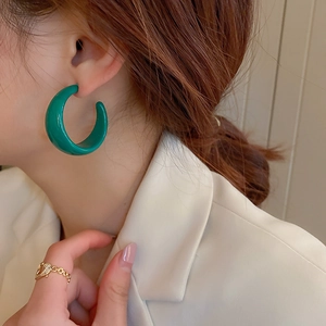 Close-up of a glossy green C-shaped resin hoop earring on model with golden heart ring
