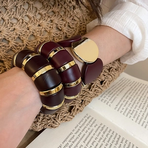 Close-up of burgundy acrylic oval stretch bracelet with gold metal accents on wrist