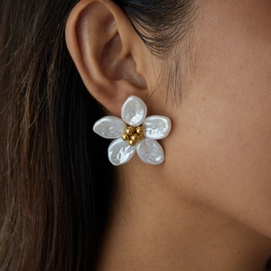 Detail of flower-shaped pearl stud earring with golden center on model's ear