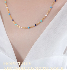 Detail of a gold plated necklace with blue and white enamel beads on a white shirt