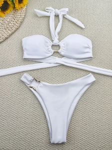 Flat lay of white two-piece bikini with gold ring hardware on beige textured background