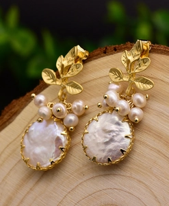 Macro detail of Baroque pearl earrings with golden leaf accents on a wood background
