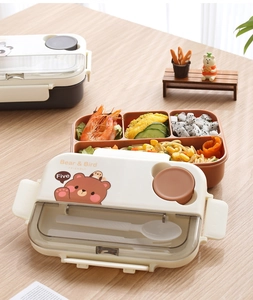 Detail of four-compartment bento box with Bear & Bird cartoon lid and spoon on wooden table