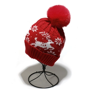 Close-up of red knit hat with white reindeer and snowflake patterns and fluffy pompom