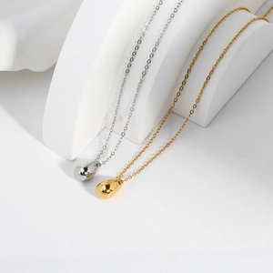 Minimalist gold and silver teardrop pendant necklace in mirror finish on white pedestals