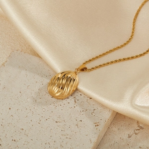 Detailed close-up of a golden teardrop pendant with wave texture on a silk and stone base