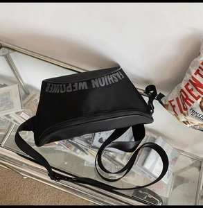 Détail du sac à bandoulière en nylon noir avec sangle ajustable et lettrage sur le devant