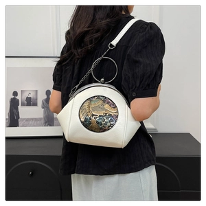 Close-up of cream white leather bag featuring antique elephant metal relief and ring handle