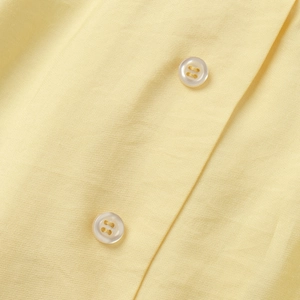 Macro view of light yellow fabric texture and four-hole white buttons on the dress placket