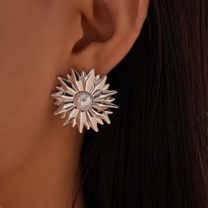 Detailed close-up of a silver sunburst stud earring with a central pearl on model's ear