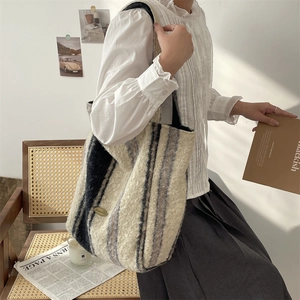 Detail of striped lamb wool tote bag showing texture and metal logo in a cozy setting