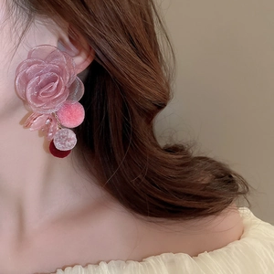 Close-up of pink organza flower earrings with fuzzy pom-pom drops on a model
