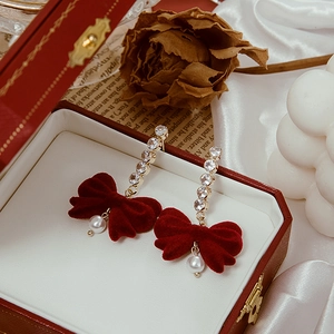 Macro shot of red velvet bow earrings with silver needles and crystal fringe detail