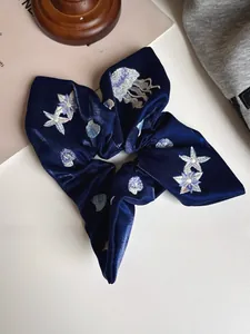 Macro detail of navy blue velvet hair scrunchie with intricate ocean creature embroidery