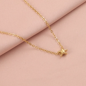 Detail shot of a golden starfish pendant necklace lying on soft pink aesthetic fabric