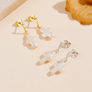 Macro shot of gold and silver S925 cross earrings with white baroque pearls
