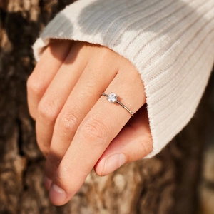 Close-up of a s925 silver round cut promise ring worn on a finger in natural sunlight