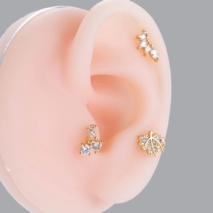 Detailed view of gold zircon stud earrings in leaf and cherry shapes on an ear model