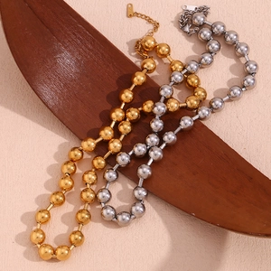 Détail de colliers à billes en or 18 carats et argent avec fermoir mousqueton sur bois