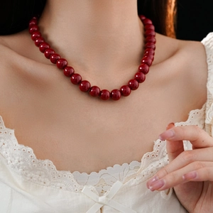 Close-up of a red round glass bead necklace worn by a model on a black background