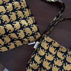 Détail du motif d'éléphant doré sur un sac en toile noire avec étiquette de marque tissée