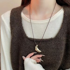 Detail of a golden croissant pendant on a brown leather cord against a knit vest