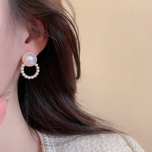 Close-up of pearl stud earring set with gold accents worn by a model in warm light