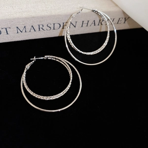 Detail view of silver triple-layered hoop earrings with twisted rope texture on a black background