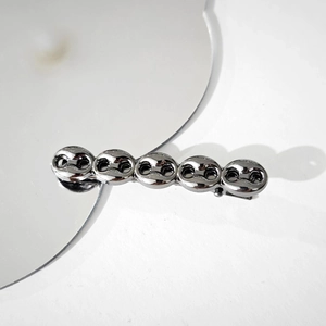 Macro detail of high-quality dark grey metallic chain design hair clip on reflective surface