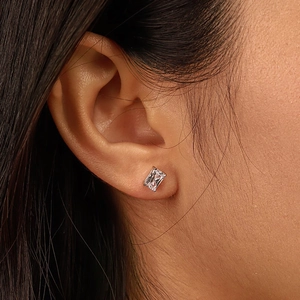 Detail of a rectangular cut zircon stud earring in a silver setting worn on ear