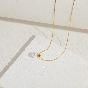 Detail of white pearl pendant on gold titanium chain over minimalist stone block