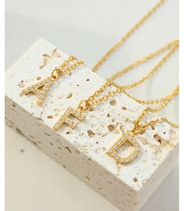 Detail of gold zircon initial necklaces featuring A, F, and D letter pendants on stone