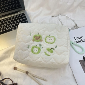 Close-up of cream quilted cosmetic bag with green apple embroidery and heart stitching