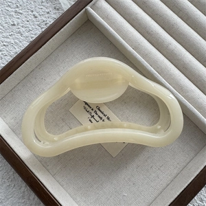 Close-up of a cream resin shark hair claw clip on a wooden display tray with soft fabric