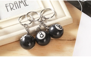 Detailed view of three resin number 8 billiards keychains on a rustic wood background
